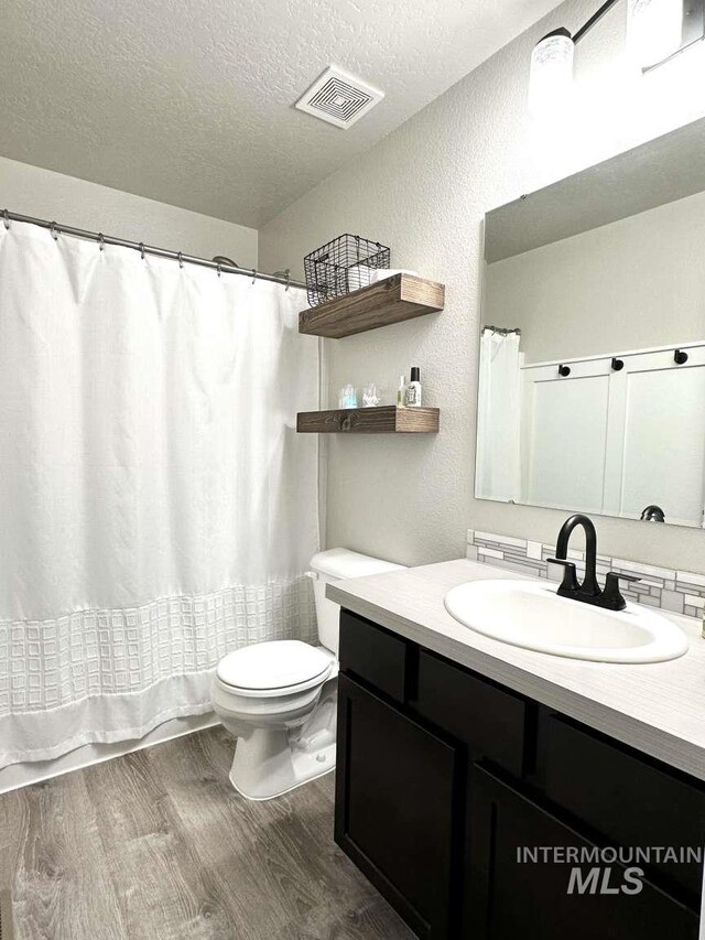 bathroom featuring toilet, a shower with curtain, wood-type flooring, vanity, and a textured ceiling