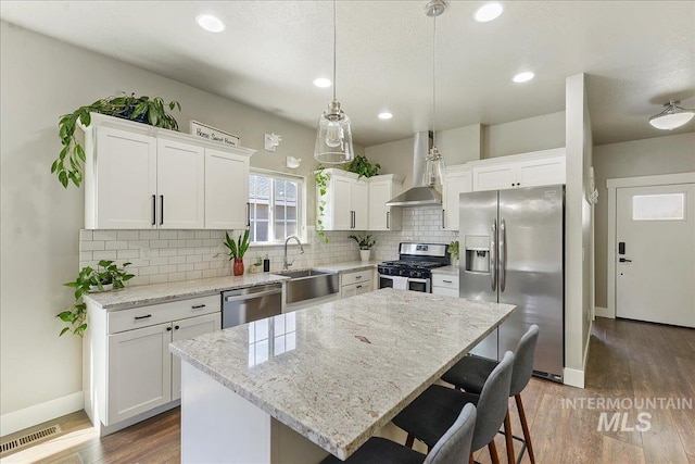 kitchen featuring white cabinets, wall chimney exhaust hood, dark wood-type flooring, stainless steel appliances, and a sink