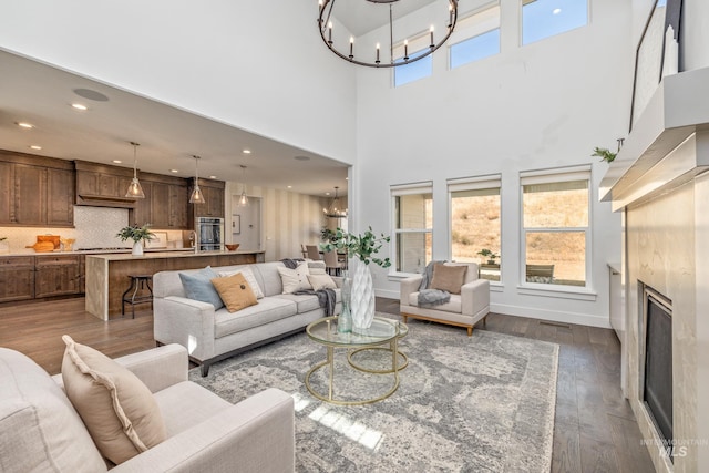 living room with an inviting chandelier, a towering ceiling, dark wood-type flooring, and a high end fireplace