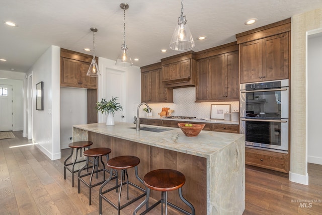 kitchen featuring light stone countertops, hardwood / wood-style flooring, stainless steel appliances, and sink