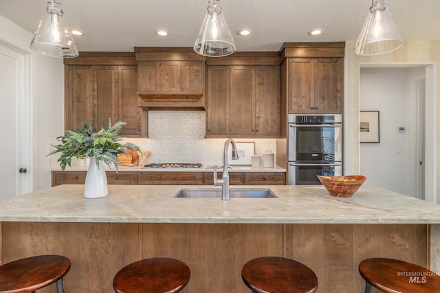 kitchen with hanging light fixtures, a large island with sink, stainless steel appliances, and tasteful backsplash