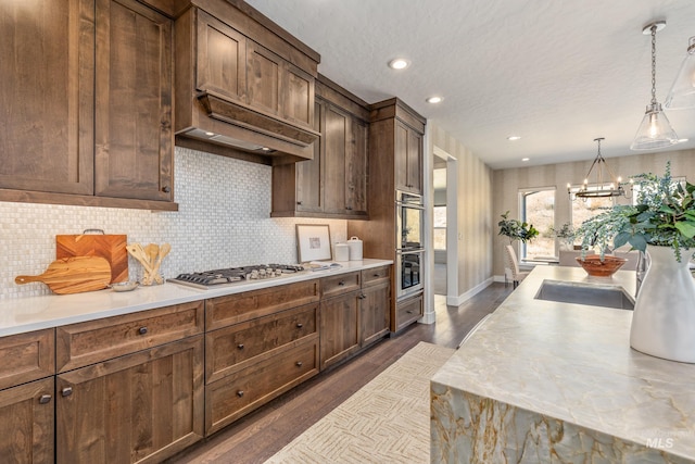 kitchen with decorative light fixtures, dark wood-type flooring, appliances with stainless steel finishes, an inviting chandelier, and decorative backsplash