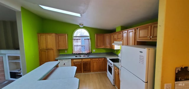 kitchen featuring white appliances, a sink, light wood-style floors, under cabinet range hood, and lofted ceiling with skylight