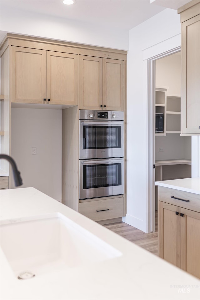 kitchen with light countertops, light brown cabinetry, double oven, a sink, and light wood-type flooring