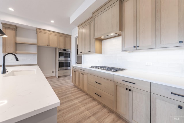 kitchen featuring stainless steel appliances, a sink, light wood-type flooring, light brown cabinetry, and tasteful backsplash