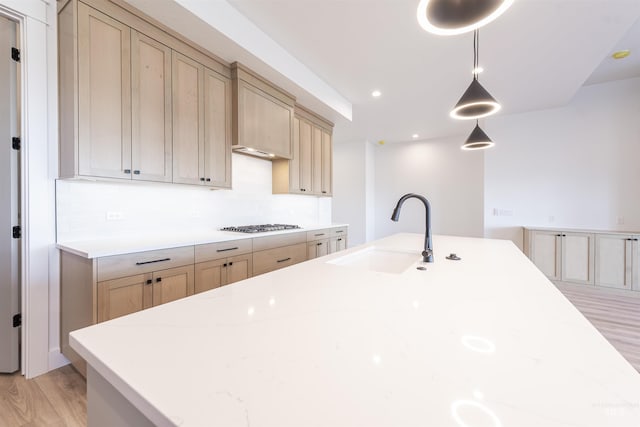 kitchen featuring gas cooktop, a sink, light wood-style floors, hanging light fixtures, and light brown cabinetry