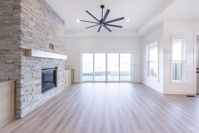 unfurnished living room with light wood-type flooring, baseboards, and a stone fireplace