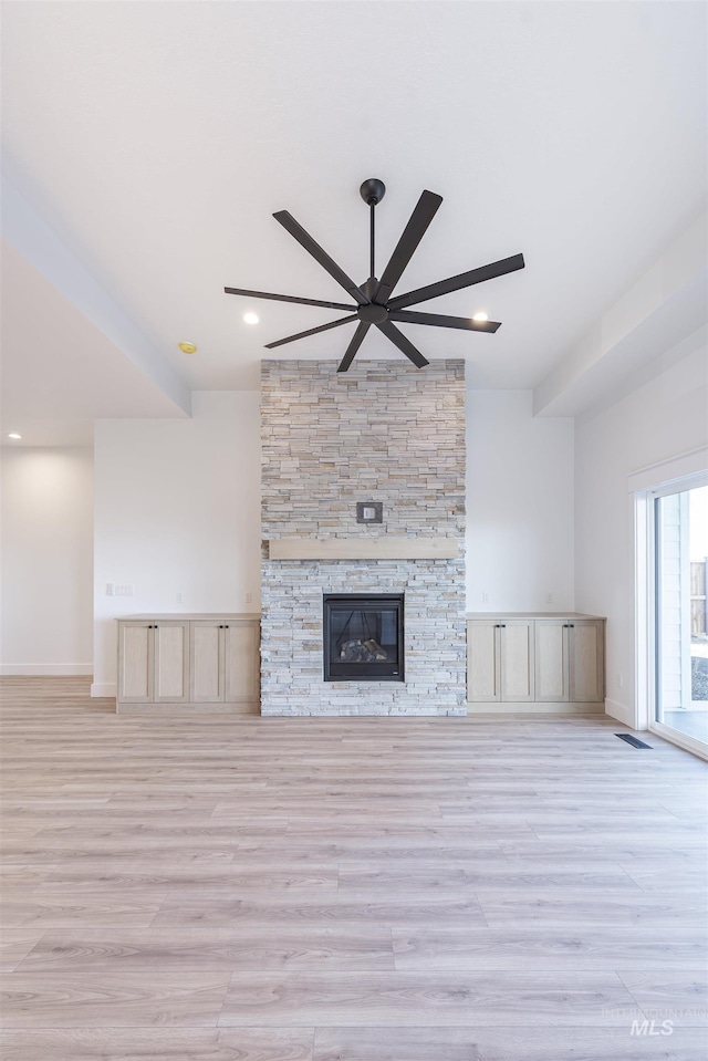 unfurnished living room featuring light wood finished floors, baseboards, visible vents, ceiling fan, and a stone fireplace