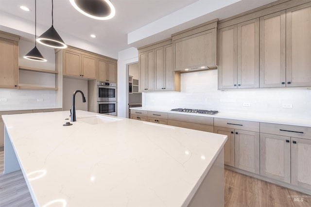 kitchen featuring double oven, gas cooktop, a sink, light wood finished floors, and a center island with sink