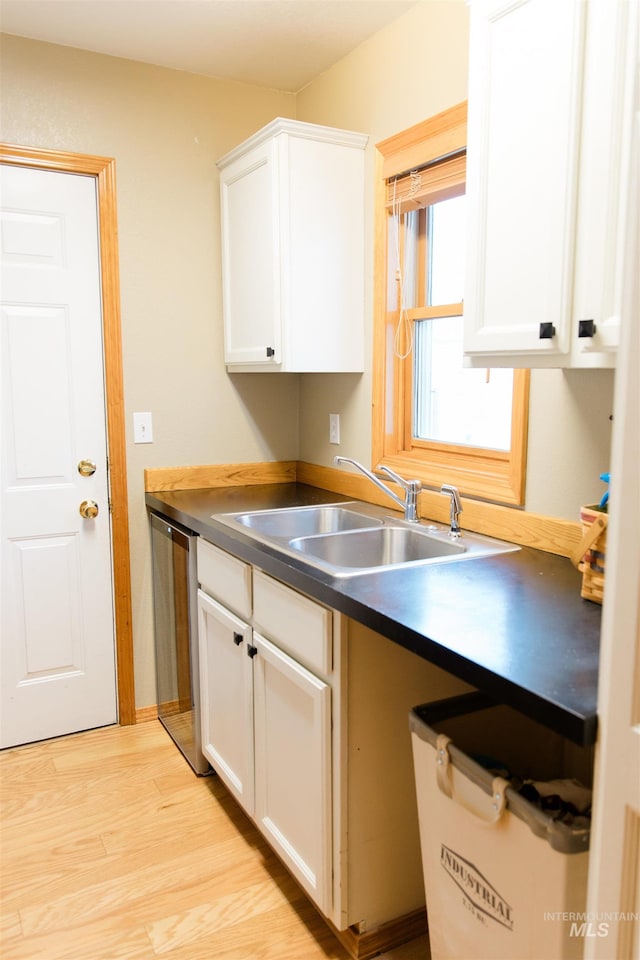 kitchen featuring stainless steel dishwasher, white cabinetry, sink, and light hardwood / wood-style flooring