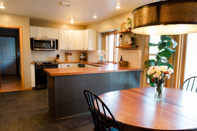 kitchen with white cabinetry, sink, tasteful backsplash, kitchen peninsula, and appliances with stainless steel finishes