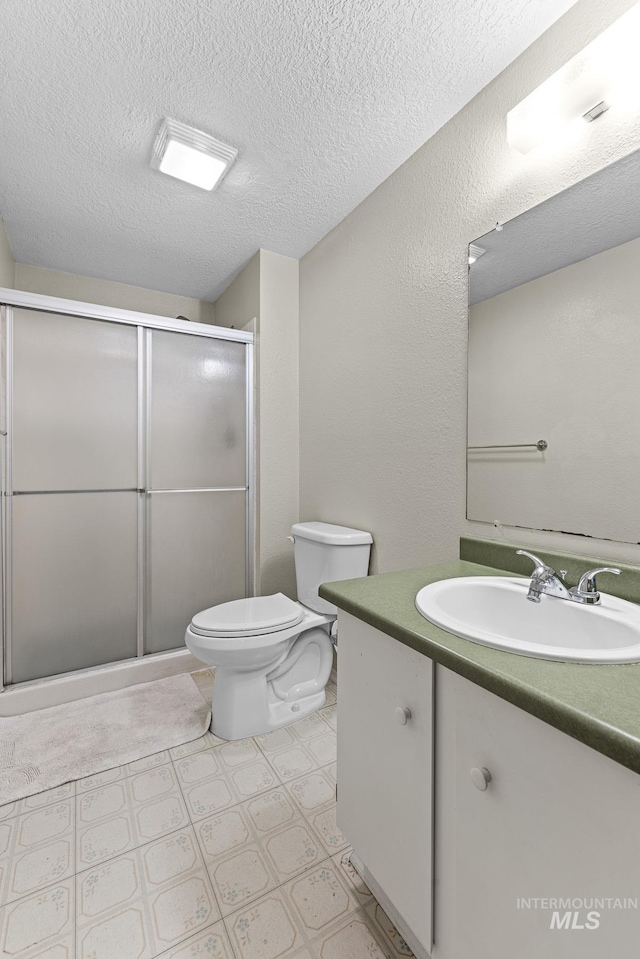 bathroom featuring toilet, a stall shower, vanity, a textured ceiling, and tile patterned floors