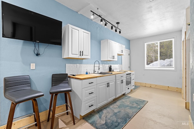 kitchen with a sink, wood counters, baseboards, white cabinetry, and backsplash