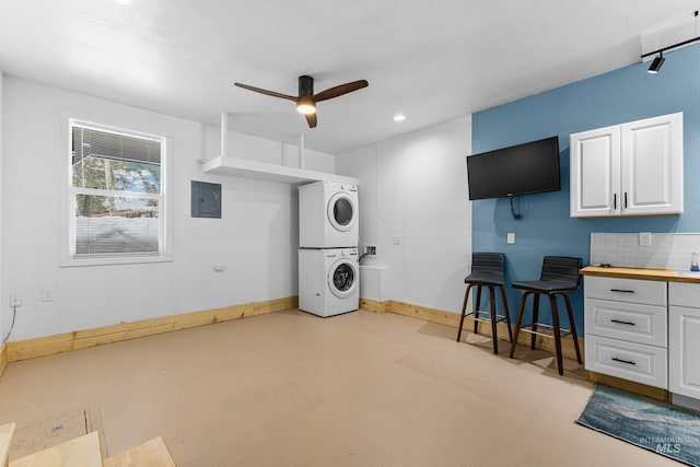 interior space featuring concrete floors, white cabinetry, baseboards, stacked washing maching and dryer, and electric panel