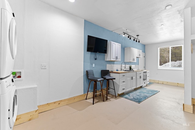 kitchen with rail lighting, finished concrete floors, stacked washer / dryer, a sink, and baseboards