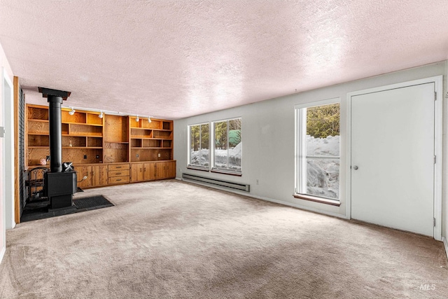 unfurnished living room with a baseboard heating unit, a wood stove, carpet flooring, and a textured ceiling