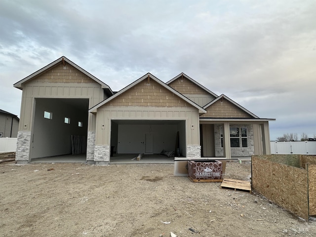 view of front of property with board and batten siding, fence, stone siding, and a garage
