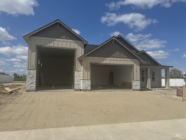 view of front of property featuring an attached garage, stone siding, board and batten siding, cooling unit, and driveway