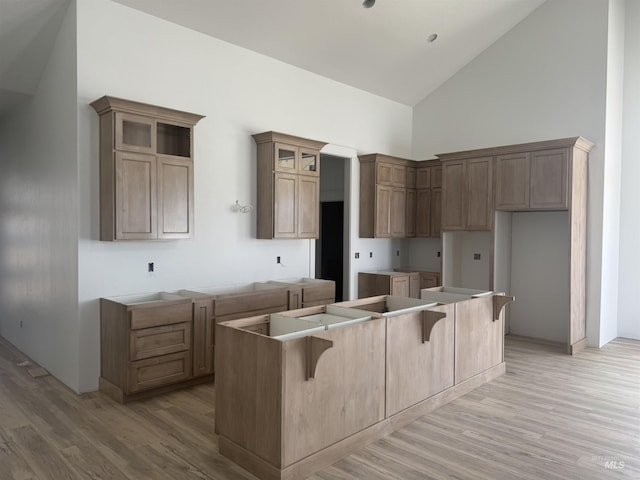 kitchen featuring glass insert cabinets, light wood-style floors, a kitchen breakfast bar, high vaulted ceiling, and a center island