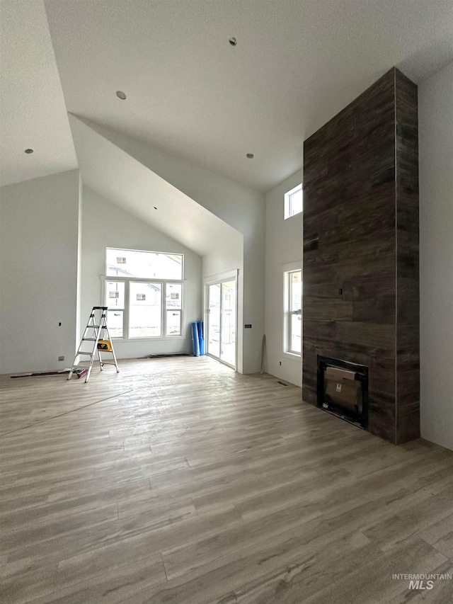 unfurnished living room with a large fireplace, high vaulted ceiling, and wood finished floors