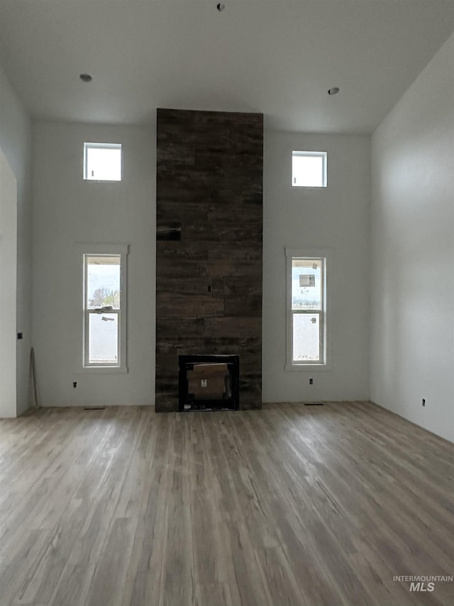 unfurnished living room featuring a towering ceiling, wood finished floors, a wealth of natural light, and a fireplace