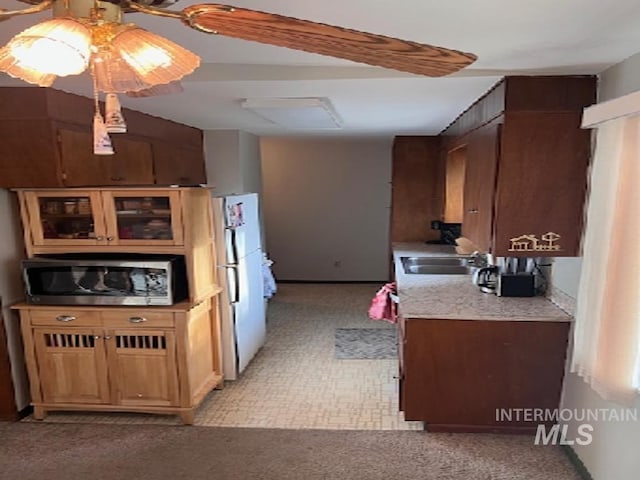 kitchen with stainless steel microwave, freestanding refrigerator, light countertops, a sink, and light carpet
