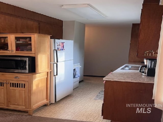 kitchen with freestanding refrigerator, stainless steel microwave, a sink, light countertops, and glass insert cabinets