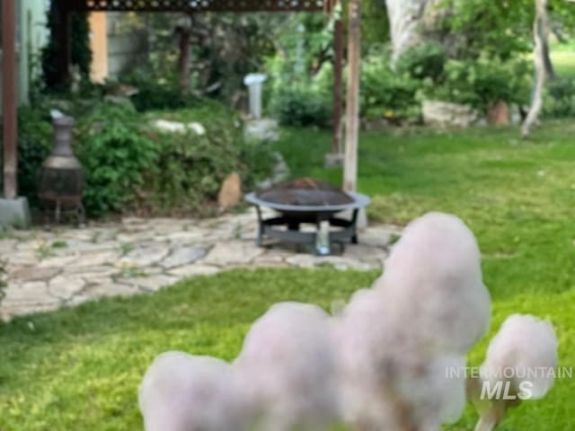 view of green lawn featuring a fire pit and a patio area