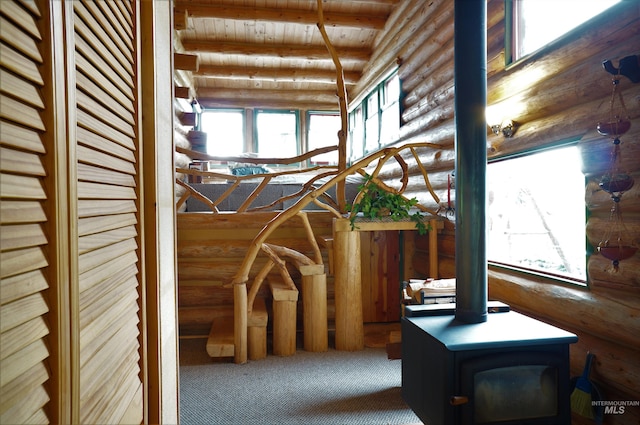 interior space featuring beamed ceiling, wooden ceiling, a healthy amount of sunlight, and a wood stove