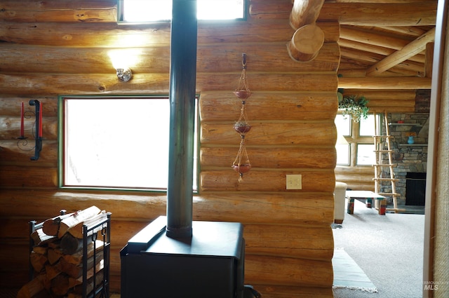 interior space with a stone fireplace, lofted ceiling with beams, wood ceiling, a wood stove, and log walls