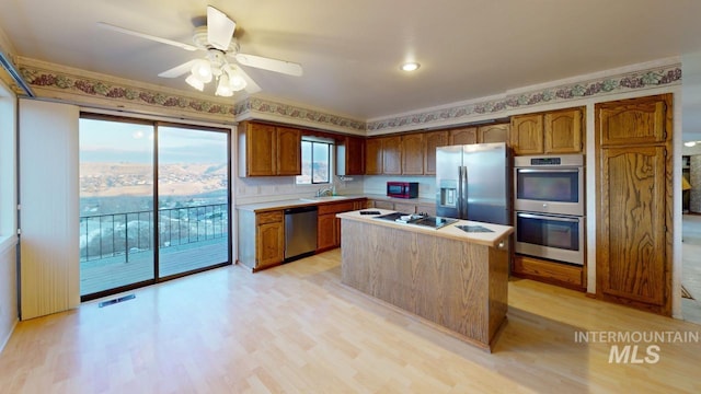 kitchen featuring sink, ceiling fan, stainless steel appliances, a kitchen island, and light wood-type flooring