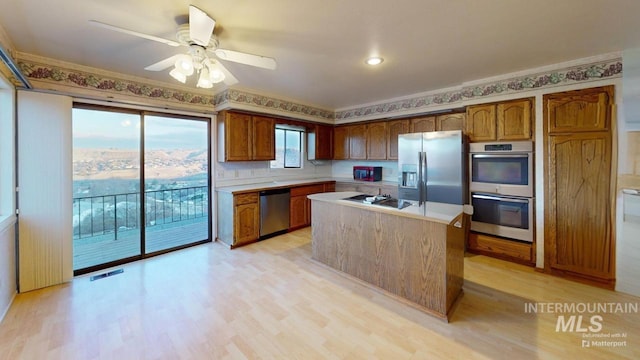 kitchen with ceiling fan, stainless steel appliances, a center island, and light wood-type flooring