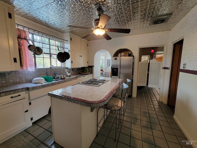 kitchen featuring ceiling fan, white cabinets, a kitchen island, tile counters, and a breakfast bar