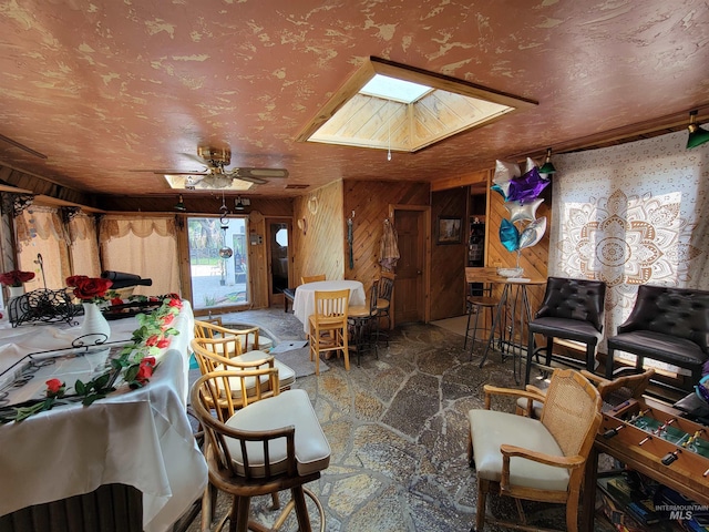 interior space with wood walls, ceiling fan, and a skylight