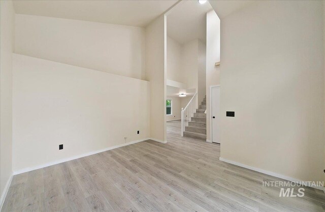 spare room featuring high vaulted ceiling, light wood-type flooring, baseboards, and stairway