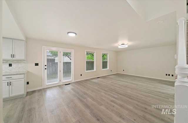 unfurnished living room featuring plenty of natural light, light wood-style floors, and baseboards