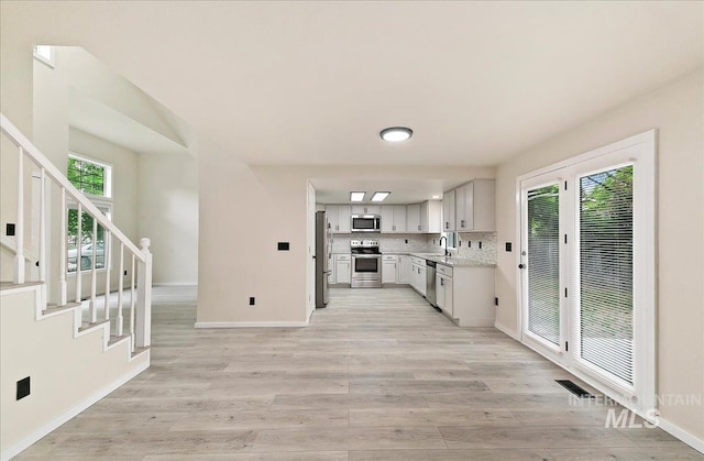 kitchen featuring appliances with stainless steel finishes, a sink, light countertops, light wood-style flooring, and tasteful backsplash