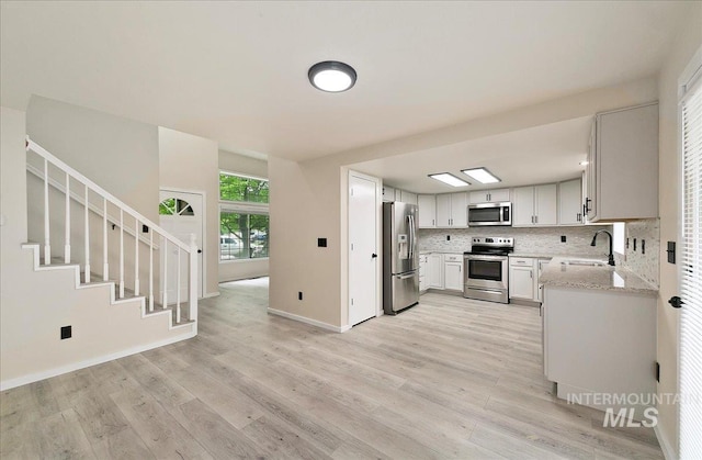 kitchen with appliances with stainless steel finishes, a sink, light wood-style floors, tasteful backsplash, and light stone counters