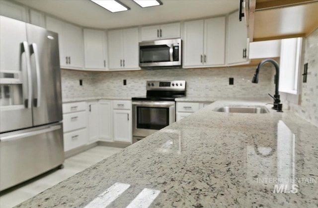 kitchen featuring stainless steel appliances, a sink, light stone countertops, white cabinetry, and tasteful backsplash