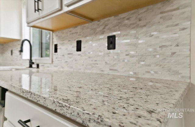 kitchen featuring backsplash, white cabinetry, light stone counters, and a sink