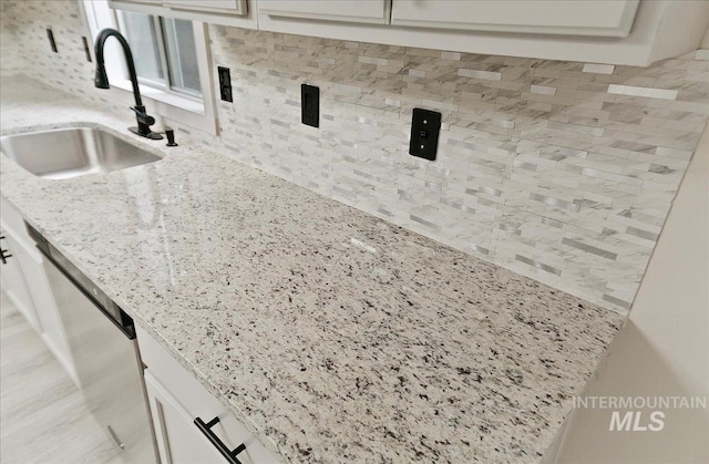 kitchen view of a sink, dishwasher, backsplash, and white cabinets