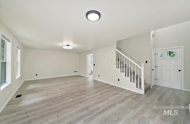 unfurnished living room with healthy amount of natural light, light wood-style floors, and stairs