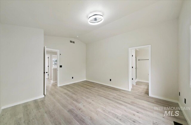 empty room with lofted ceiling, light wood-style flooring, and baseboards