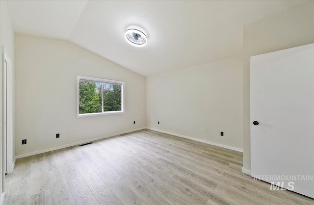empty room featuring lofted ceiling, light wood-style flooring, and baseboards