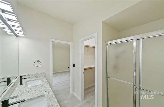 bathroom with a stall shower, wood finished floors, a spacious closet, double vanity, and baseboards