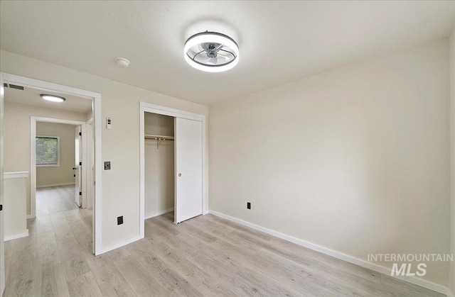 unfurnished bedroom with light wood-style floors, baseboards, and a closet