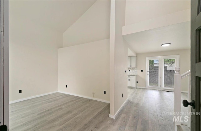unfurnished living room featuring high vaulted ceiling, light wood-style flooring, and baseboards