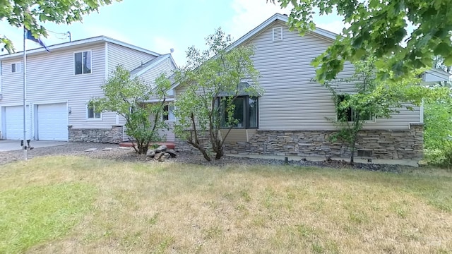 exterior space featuring stone siding, a yard, an attached garage, and driveway