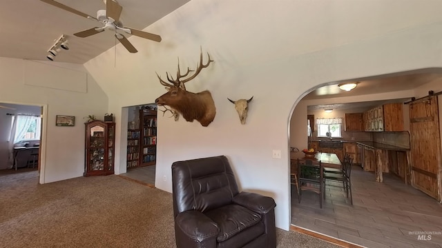 living room with arched walkways, lofted ceiling, light colored carpet, a barn door, and a ceiling fan