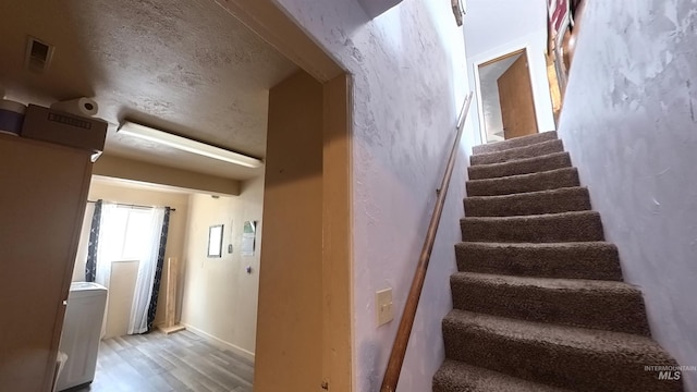 staircase with a textured ceiling, wood finished floors, and visible vents